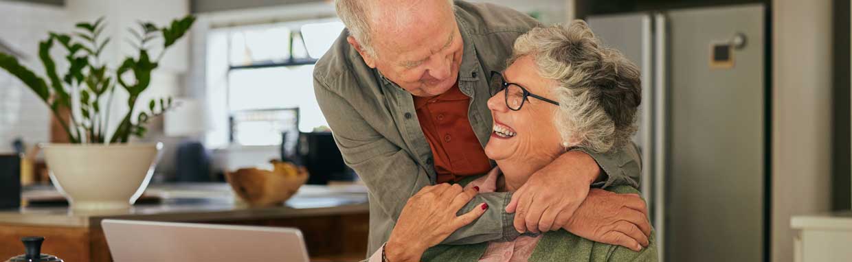 Retirement age couple hugging and looking at a laptop